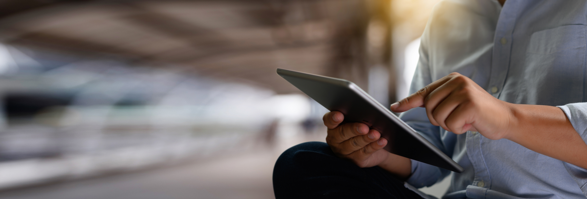 Lässig sitzender Mann, der an einem Bahnhof auf einen Tablet-Bildschirm tippt.